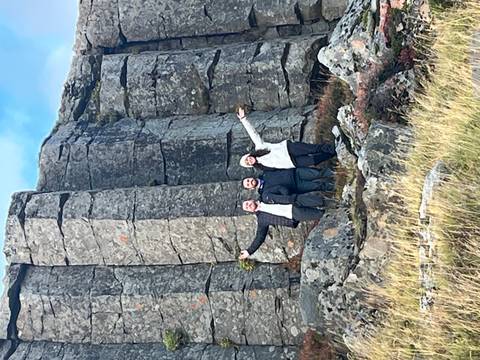 Three people in front of basalt columns with joyful poses.