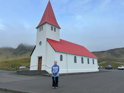 Person standing in front of a white church with a red roof.