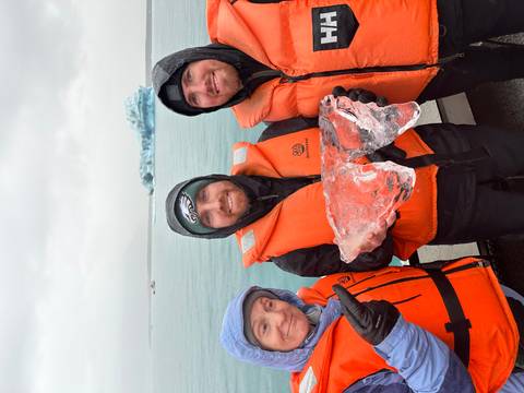 Group posing with an ice chunk on a boat in cold weather.