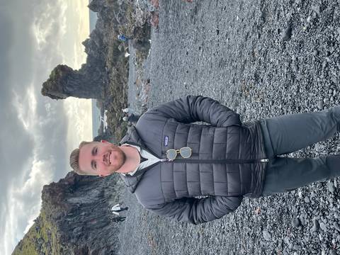 Person standing on a rocky beach with a large rock formation in the background.