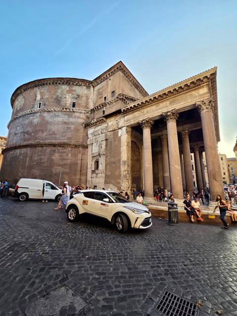 The Pantheon in Rome with parked cars and people around.