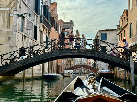 Gondolas under a bridge with people walking above in Venice.