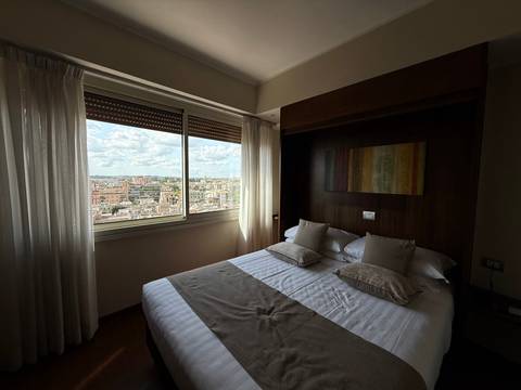 A hotel room with a double bed and a window view of the city skyline.
