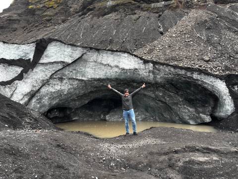 Person standing triumphantly in front of glacier entrance.