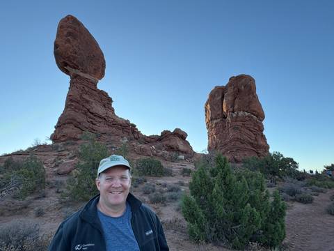 Man posing in front of balancing rock formations.