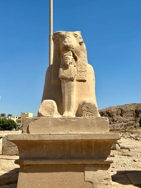 Ancient Egyptian statue under a clear blue sky.