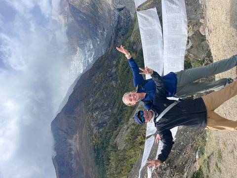 Two hikers posing with prayer flags and mountains in the background.