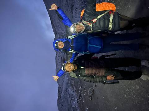 Three people in warm clothing on a mountain trail, smiling and posing at dusk.