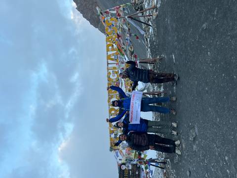 Four people with a sign 'Annapurna Circuit' at a mountain pass covered in prayer flags.