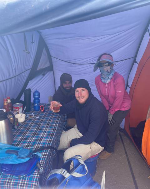 Three people inside a tent, with one holding a drink.