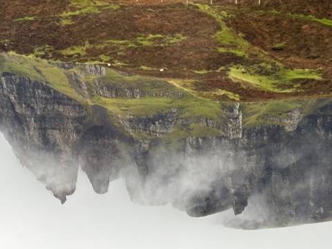 Misty mountain peaks with green grass, possibly in Scotland.