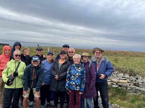 Group photo of smiling tourists in outdoor attire by a stone fence.