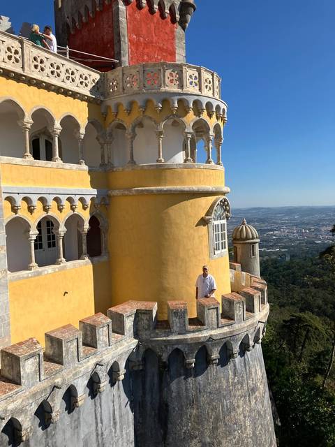 Person standing on the balcony of a yellow towered building with a scenic view.