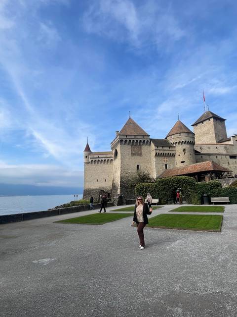 Person posing in front of a lakeside castle.