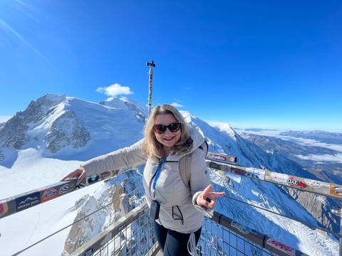 Person posing on a snowy mountain peak with blue sky.