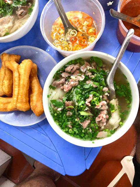 Bowl of Pho with meat, greens, and accompanying fried dough sticks.