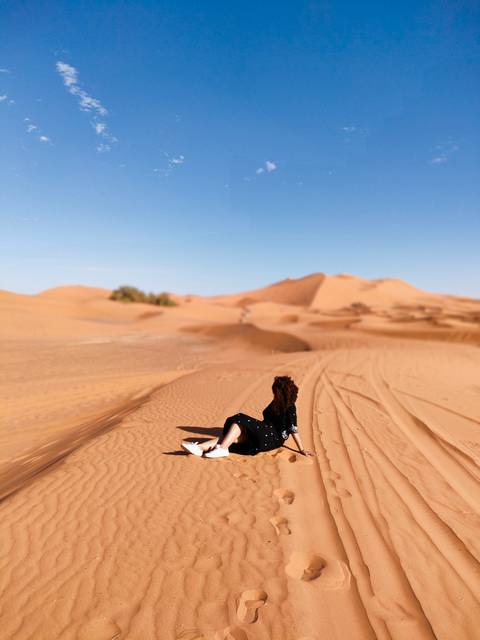 Person sitting on sand dunes in a desert.