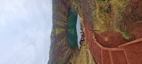 Crater with a lake at the bottom and people hiking down.
