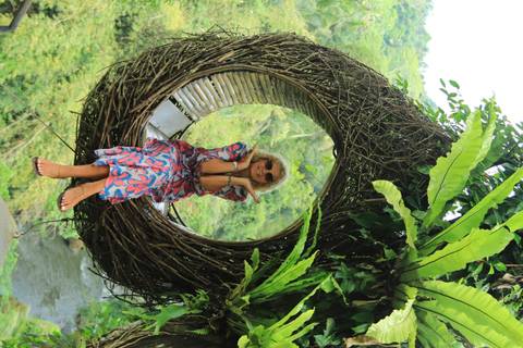 Woman sitting in a hanging nest-style seat with a lush view.