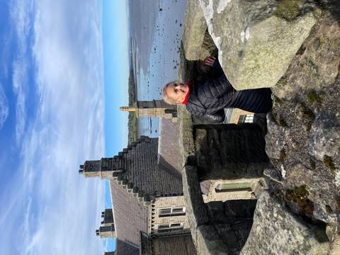 Woman standing on a castle-like structure with a coastal view.