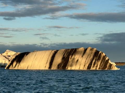 Iceberg with black streaks floating in the water.