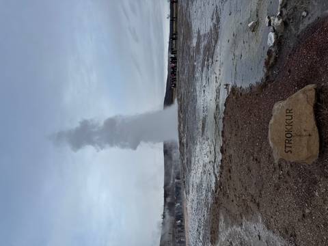 Geyser eruption with onlookers in the distance.