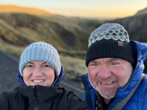 Couple wearing winter hats, smiling with scenic views in the background.
