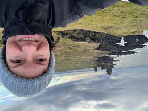Woman taking a selfie with a coastal rock formation in the background.