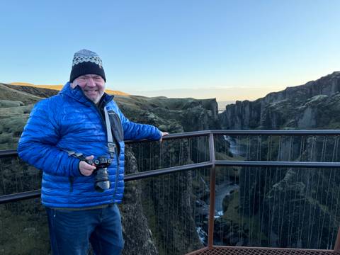 Man in blue jacket posing with a camera on a viewing platform overlooking a canyon.