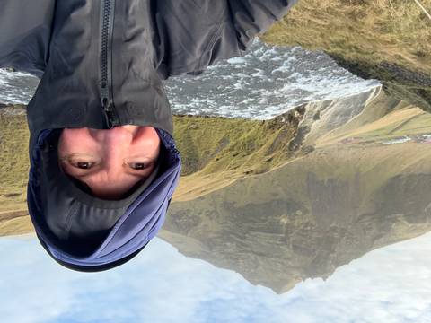Woman dressed warmly, landscape with a mountain and waterfall in the background.