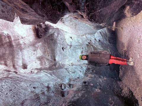 Woman inside an ice cave, warmly dressed and smiling.