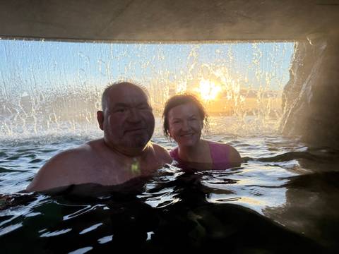 Couple enjoying a hot spring with water cascading behind them.