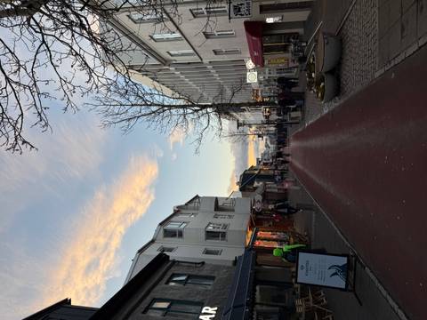 Street view with people walking, shops, and sunset sky.