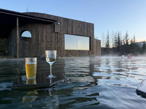 Drinks on a floating platform in a hot spring with a wooden building in the background.