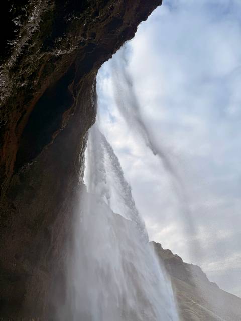 View from behind a waterfall, looking up at the cascading water.