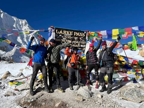 Group of trekkers celebrating at Larke Pass with colorful prayer flags.