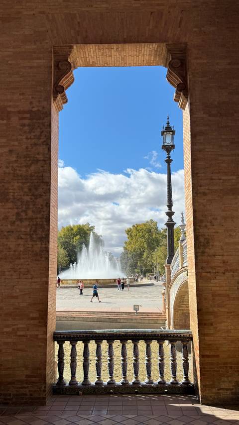 Fountain and lamp post viewed through a large brick archway.