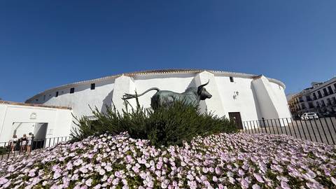 Statue of a bull in front of a white bullring with flowers.