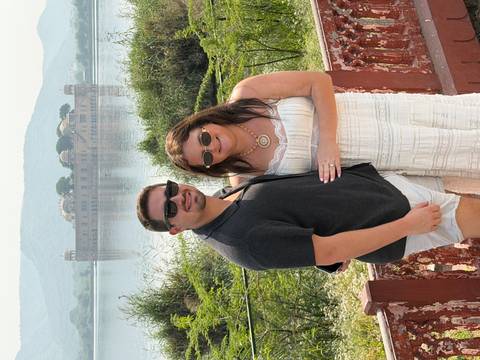 Couple standing in front of a lake with a building in the background.