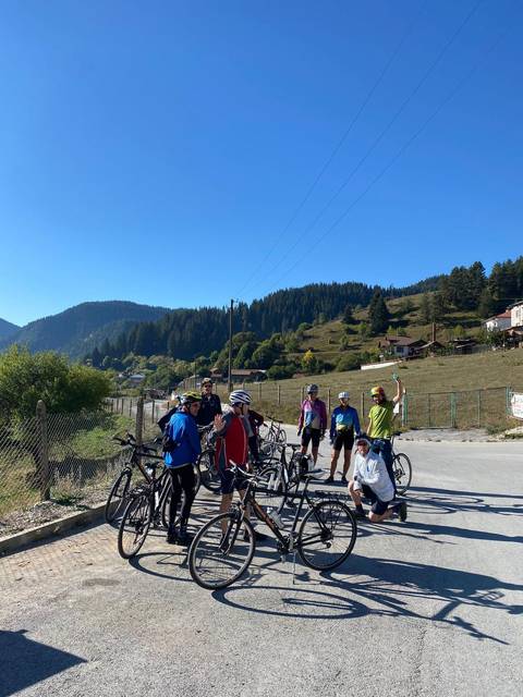 Group of cyclists gathered beside a road in a hilly area.