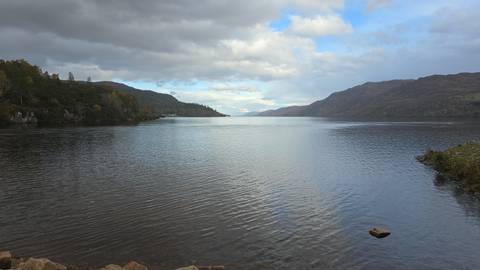 Calm lake with hills in the background under cloudy sky.