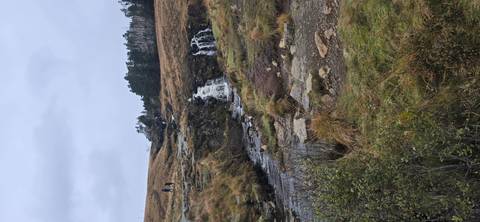 Small waterfall in a grassy landscape with hikers.