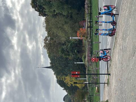 A park with electric scooters and a tall spire in the background.
