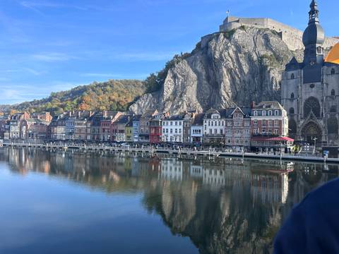 Colorful buildings along a river with a hill and church.