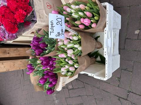 Bunches of tulips wrapped in brown paper, displayed in a market.