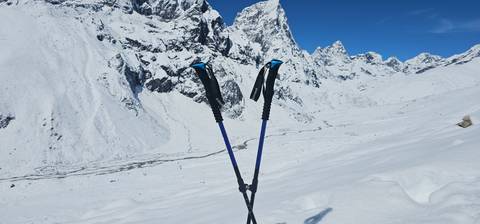 Trekking poles standing in the snow against a backdrop of snowy mountains.