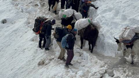 Group of people with yaks carrying loads in snow.