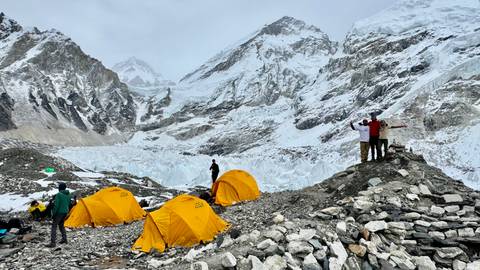 Snow camp with yellow tents and mountains in the background.