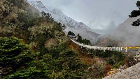 Suspension bridge in a mountainous landscape with prayer flags.