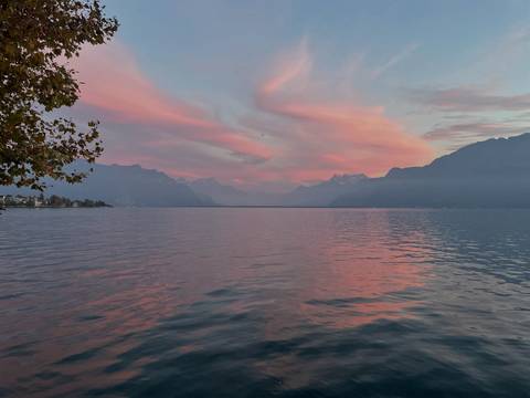 A lake with mountains in the distance and a pink sunset sky.